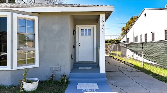 doorway to property featuring fence, a chimney, and stucco siding