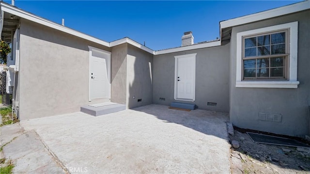 doorway to property featuring crawl space, stucco siding, a patio area, and a chimney