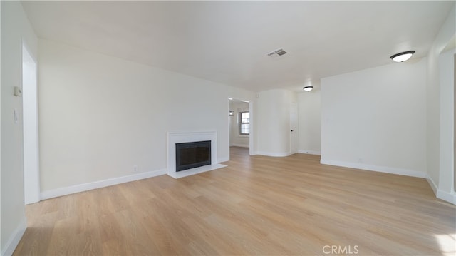 unfurnished living room with a fireplace with flush hearth, baseboards, light wood-type flooring, and visible vents