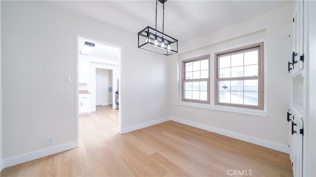 unfurnished dining area with a notable chandelier, light wood-type flooring, and baseboards