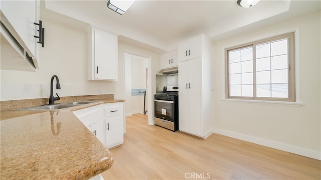 kitchen featuring a sink, under cabinet range hood, white cabinetry, light wood finished floors, and stainless steel gas range