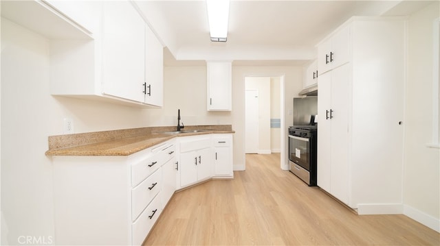 kitchen featuring under cabinet range hood, a sink, gas stove, light wood-style floors, and white cabinets