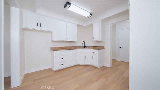 kitchen featuring white cabinetry, baseboards, light wood-type flooring, and a sink