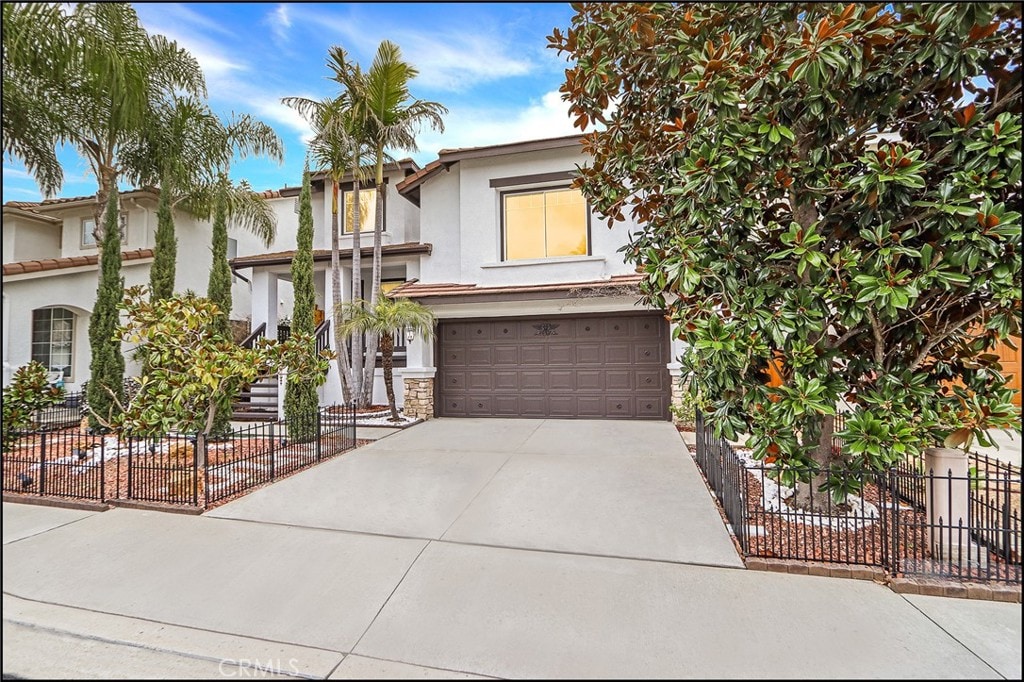 view of front facade with stucco siding, a garage, concrete driveway, and fence