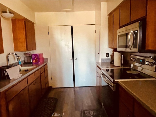 kitchen with brown cabinets, appliances with stainless steel finishes, dark wood-type flooring, and a sink