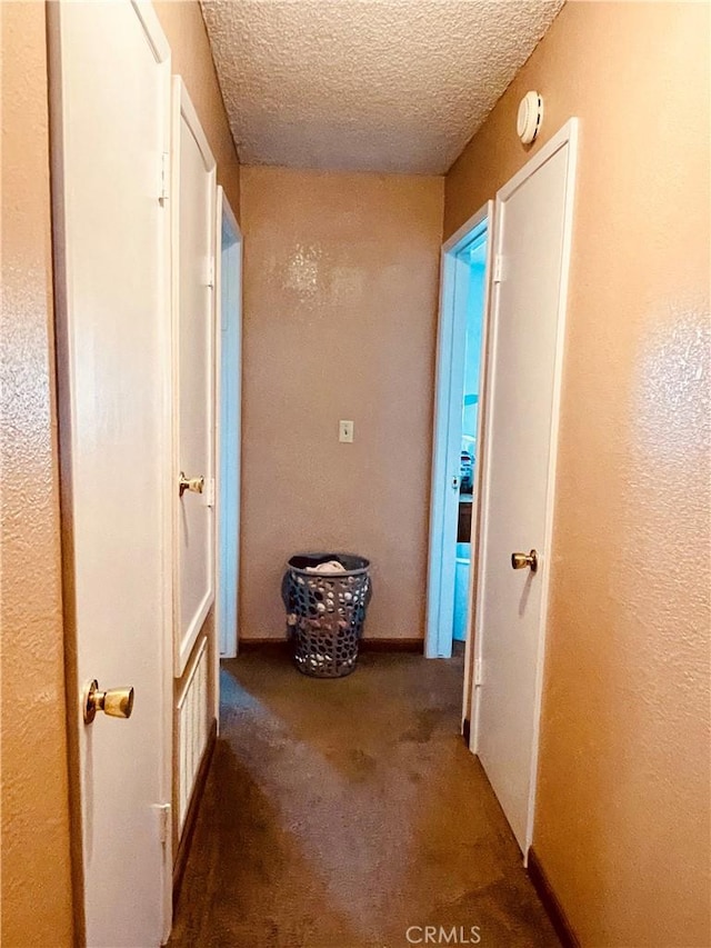 hallway featuring carpet flooring, baseboards, and a textured ceiling