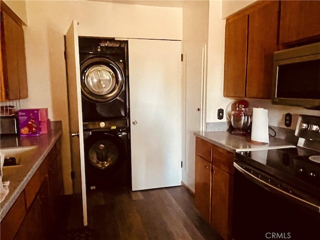 kitchen with electric range, brown cabinets, stacked washer and dryer, stainless steel microwave, and dark wood finished floors