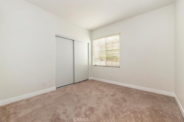 unfurnished bedroom featuring baseboards, light carpet, and a closet