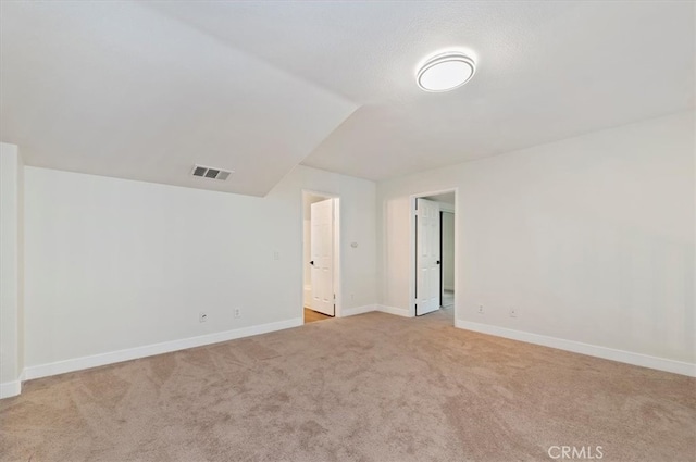 empty room featuring visible vents, light carpet, baseboards, and vaulted ceiling