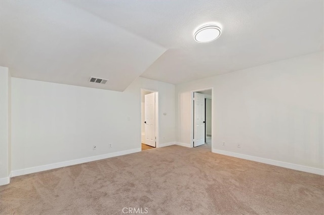 empty room with lofted ceiling, light colored carpet, visible vents, and baseboards