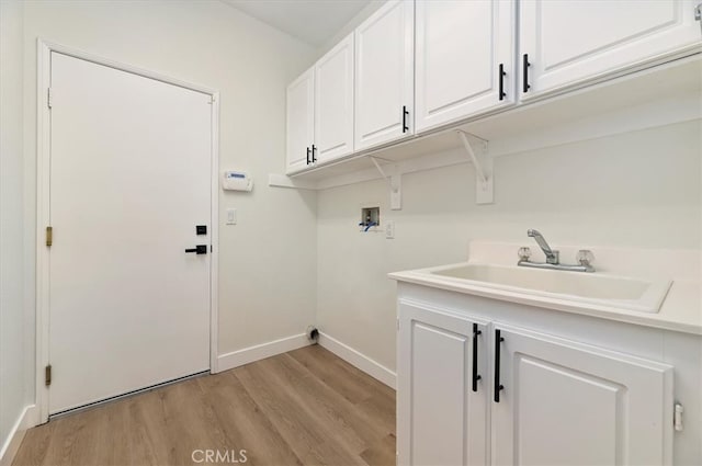 clothes washing area with light wood-type flooring, washer hookup, a sink, cabinet space, and baseboards