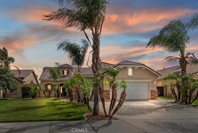 mediterranean / spanish house with a tiled roof, concrete driveway, a front yard, stucco siding, and a garage