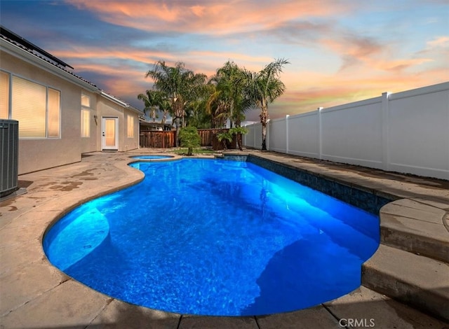 pool at dusk featuring a patio, a fenced in pool, a fenced backyard, central AC, and an in ground hot tub