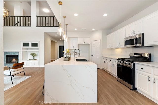 kitchen featuring recessed lighting, light stone counters, stainless steel appliances, a sink, and light wood-type flooring