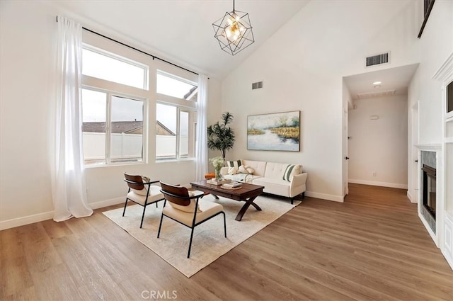 living area with a glass covered fireplace, visible vents, baseboards, and light wood-style flooring