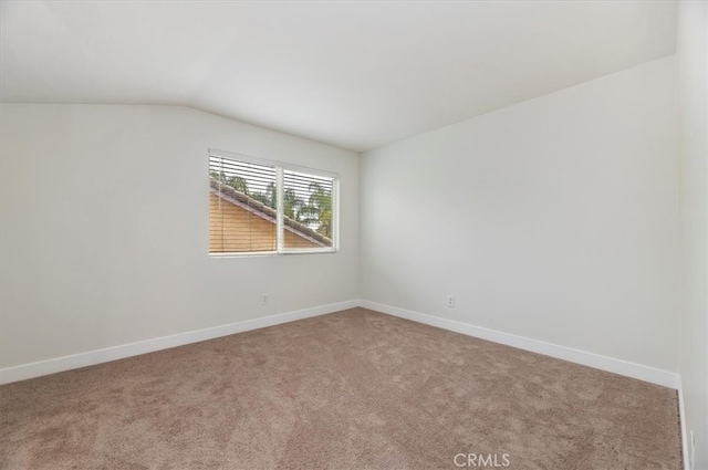 carpeted spare room with vaulted ceiling and baseboards