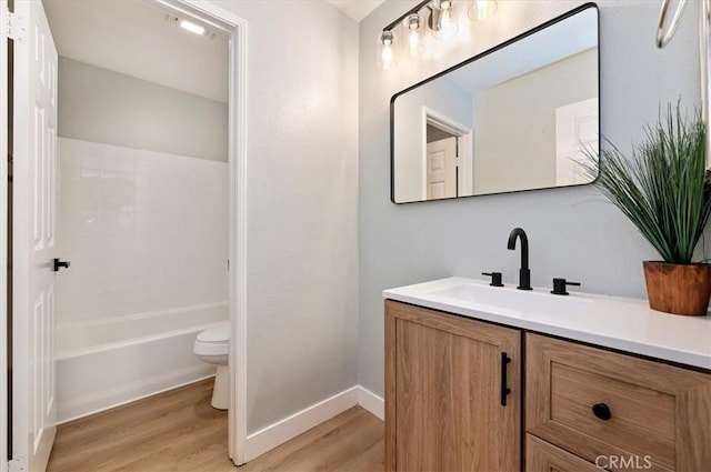 bathroom with vanity, toilet, baseboards, wood finished floors, and  shower combination