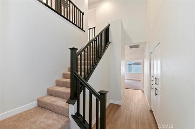 stairs featuring a towering ceiling, visible vents, wood finished floors, and baseboards