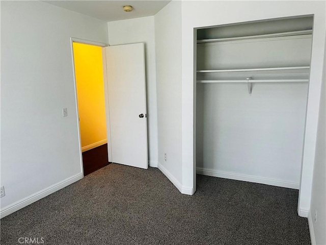 unfurnished bedroom with a closet, baseboards, and dark carpet