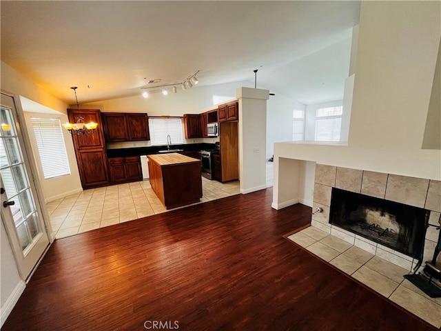 kitchen featuring a kitchen island, light wood-type flooring, vaulted ceiling, appliances with stainless steel finishes, and a sink