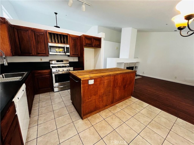 kitchen featuring vaulted ceiling, a tile fireplace, light tile patterned flooring, stainless steel appliances, and a sink