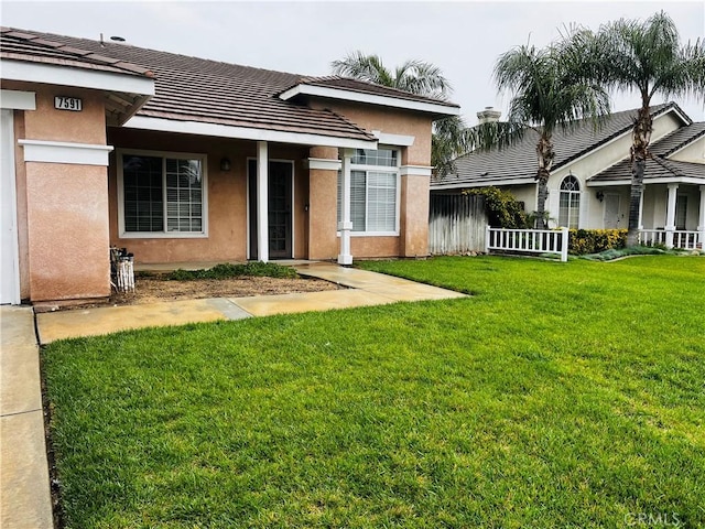 back of property with a lawn, a tiled roof, fence, and stucco siding