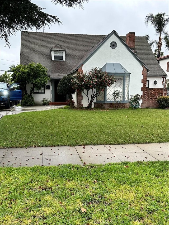 view of front of house with a front lawn, a chimney, roof with shingles, and stucco siding