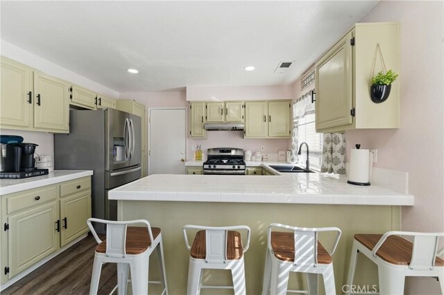 kitchen with under cabinet range hood, cream cabinets, a sink, visible vents, and appliances with stainless steel finishes