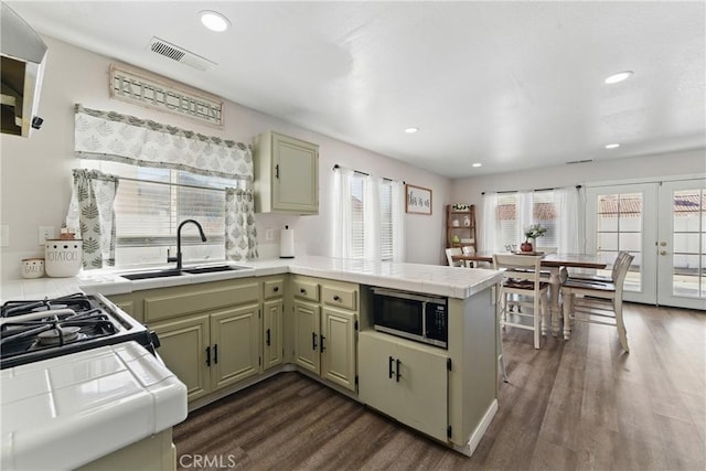 kitchen with a sink, a peninsula, stainless steel microwave, tile countertops, and visible vents