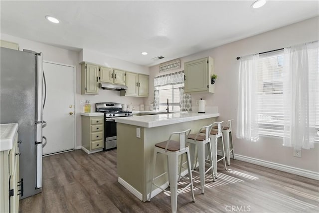 kitchen featuring a sink, a peninsula, under cabinet range hood, stainless steel appliances, and visible vents