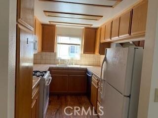 kitchen featuring brown cabinetry, freestanding refrigerator, and gas range oven