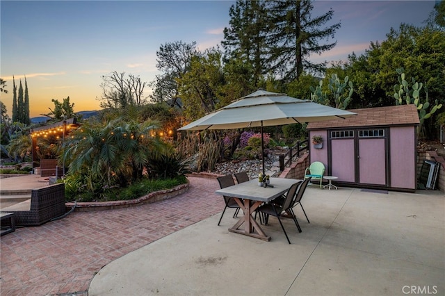 patio terrace at dusk with outdoor dining area, an outbuilding, and a shed