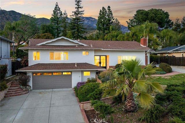 view of front of home featuring fence, concrete driveway, stucco siding, a chimney, and a mountain view