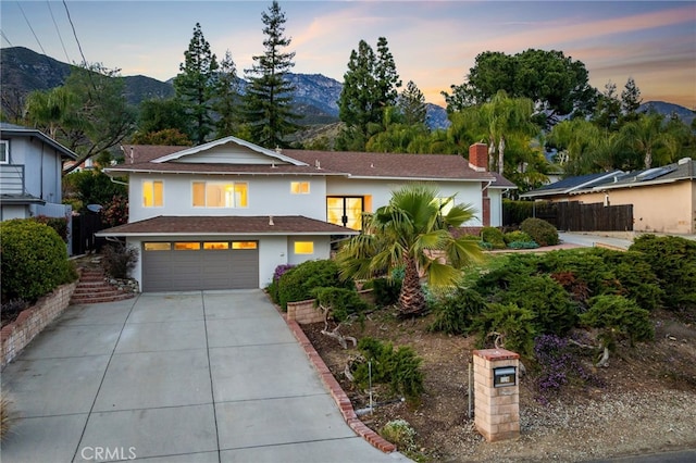 traditional-style house featuring stucco siding, driveway, a mountain view, a garage, and a chimney