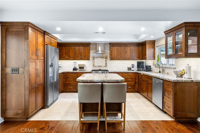 kitchen with a center island, light stone countertops, decorative backsplash, appliances with stainless steel finishes, and wall chimney exhaust hood