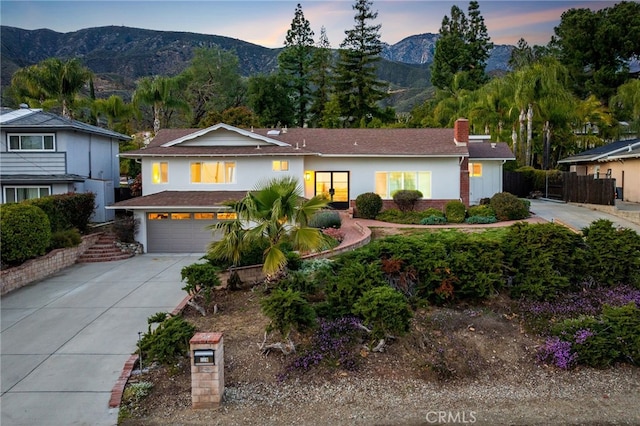 view of front facade featuring a mountain view, driveway, a chimney, and an attached garage