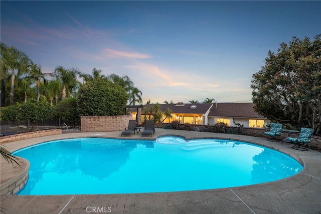 pool at dusk featuring a patio area, an outdoor pool, and fence