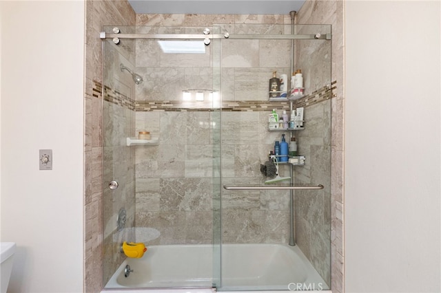 bathroom featuring combined bath / shower with glass door and toilet