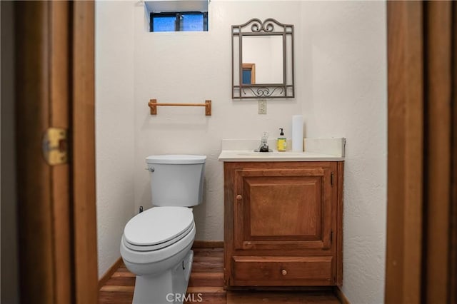 bathroom featuring toilet, wood finished floors, baseboards, vanity, and a textured wall