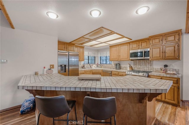 kitchen featuring tile countertops, stainless steel appliances, light wood-style floors, and a breakfast bar