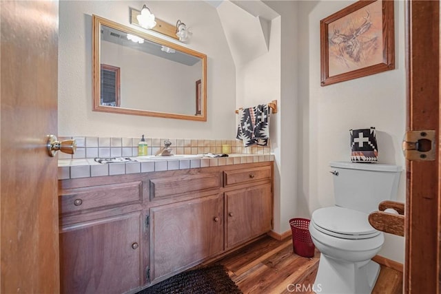 half bath featuring baseboards, toilet, wood finished floors, and vanity