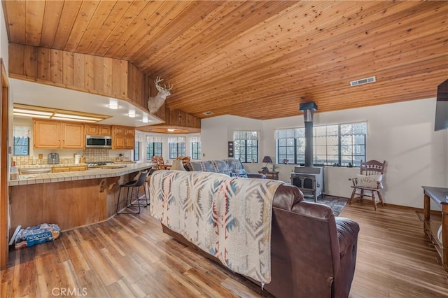 living area featuring visible vents, high vaulted ceiling, light wood-style flooring, wooden ceiling, and a wood stove