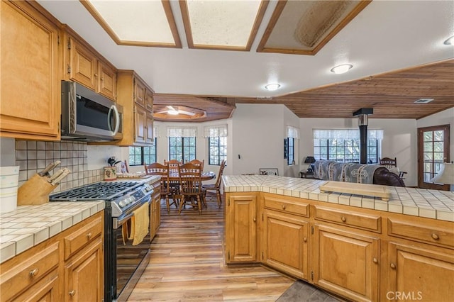 kitchen featuring tile countertops, stainless steel appliances, light wood-style flooring, and decorative backsplash