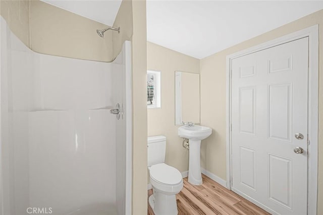 bathroom with baseboards, toilet, wood finished floors, a shower, and a sink