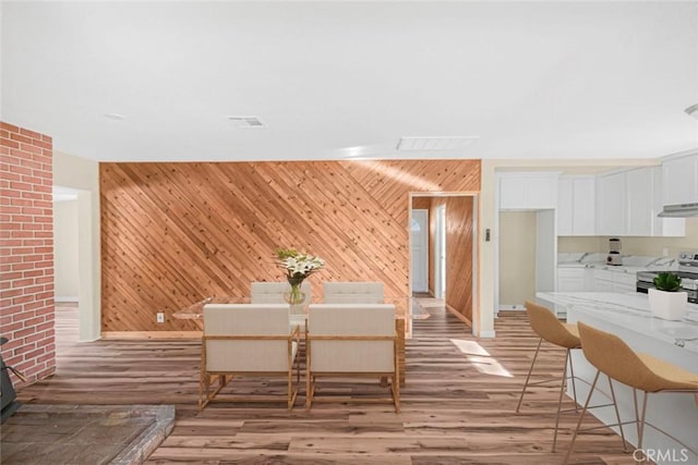 dining room with visible vents, baseboards, light wood-style floors, and wooden walls