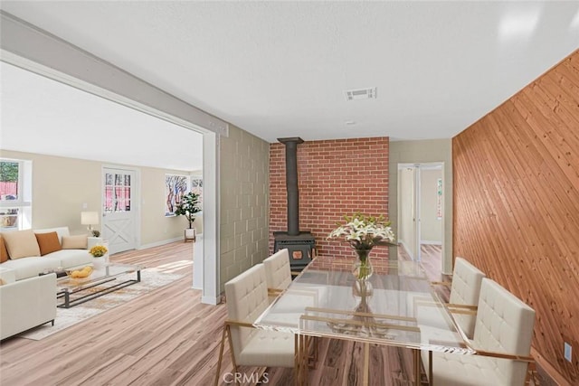 dining space with wooden walls, wood finished floors, visible vents, baseboards, and a wood stove