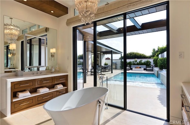 bathroom with a freestanding bath, a skylight, vanity, and a chandelier