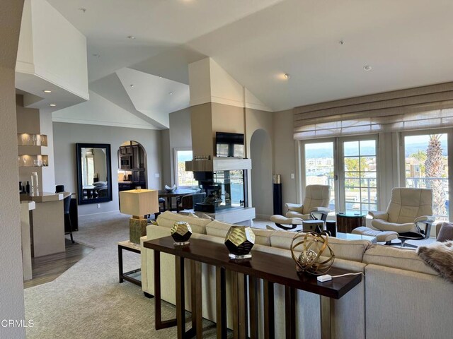 living room featuring baseboards, arched walkways, high vaulted ceiling, and light carpet