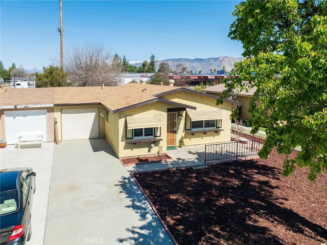 single story home with stucco siding, fence, a mountain view, concrete driveway, and an attached garage