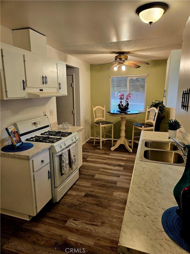 kitchen with a ceiling fan, dark wood finished floors, white range with gas cooktop, a sink, and white cabinetry